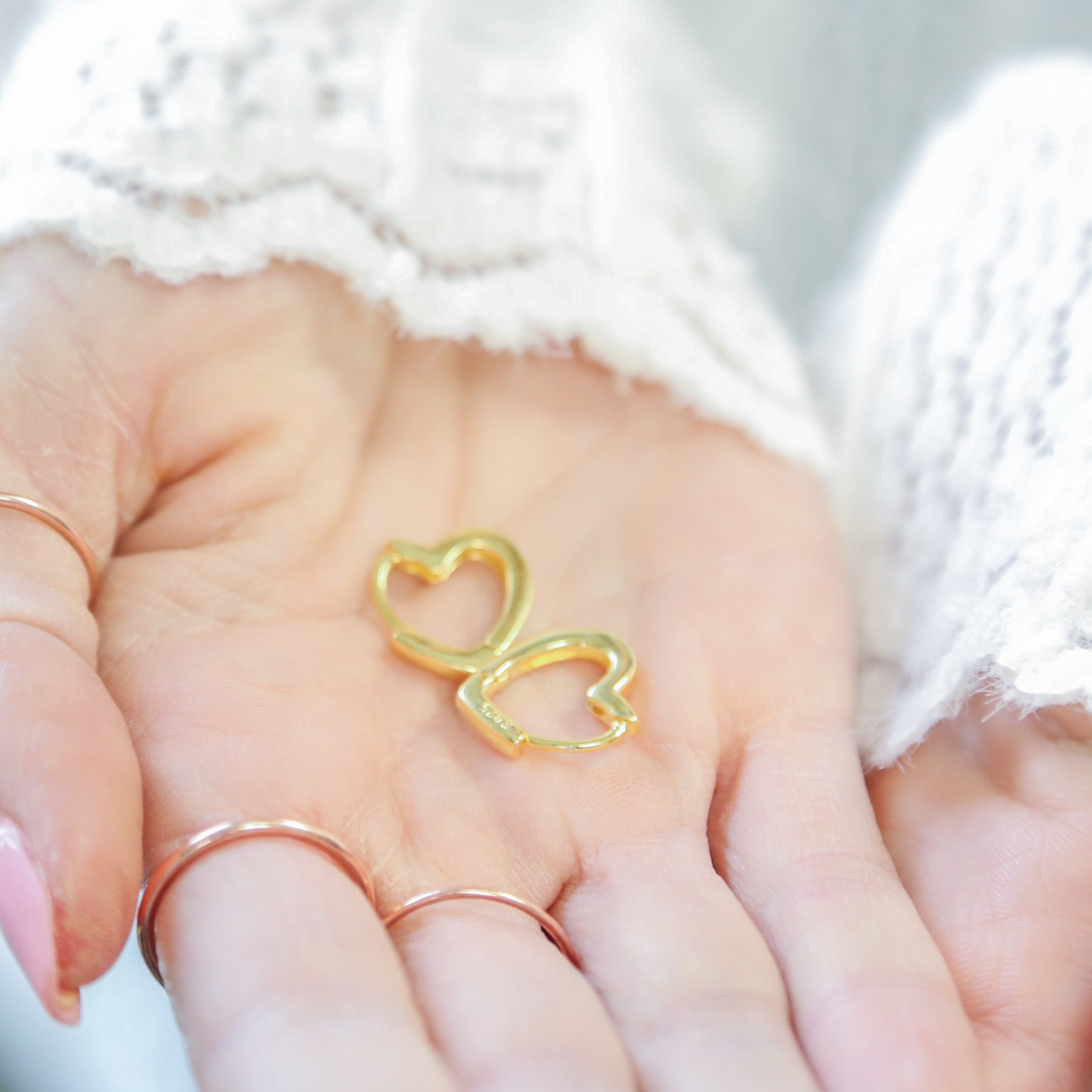 a woman's hand holding a gold heart shaped ring