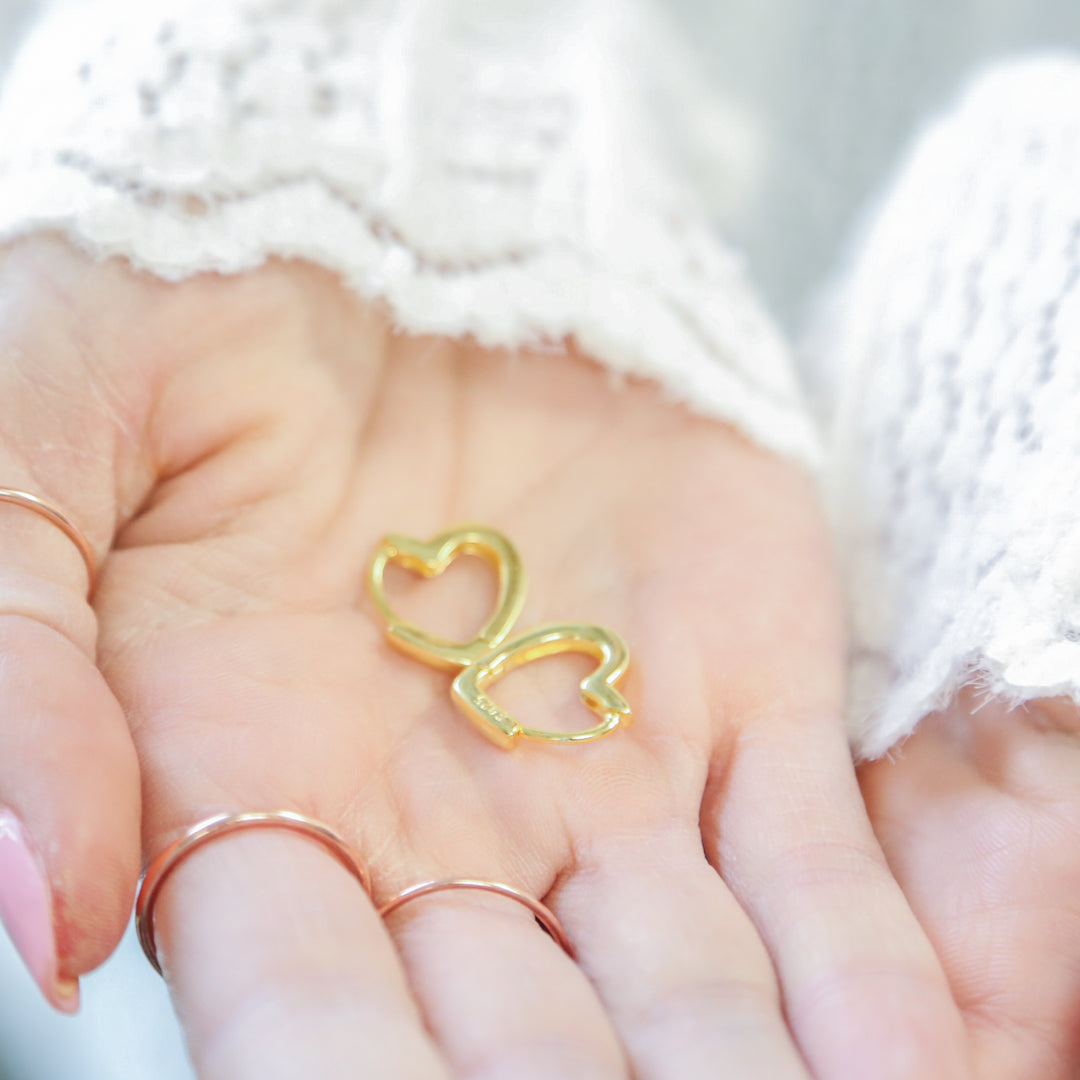 a woman's hand holding a gold heart shaped ring
