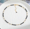 a black and gold beaded necklace on a white plate