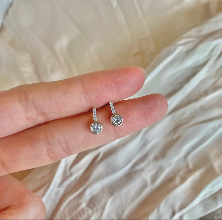 a person's hand holding a pair of diamond earrings