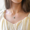 a woman wearing a necklace with a green stone