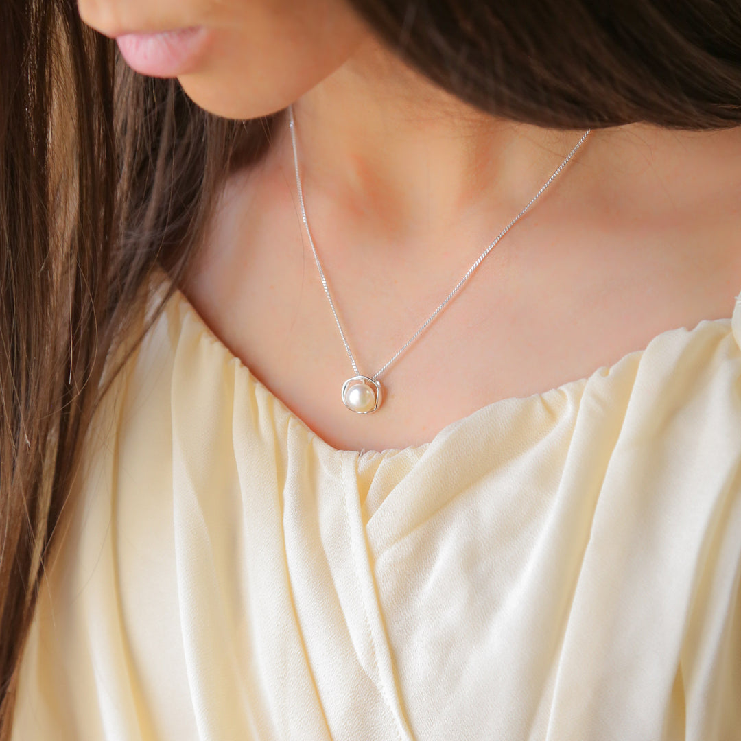 a woman wearing a necklace with a pearl on it