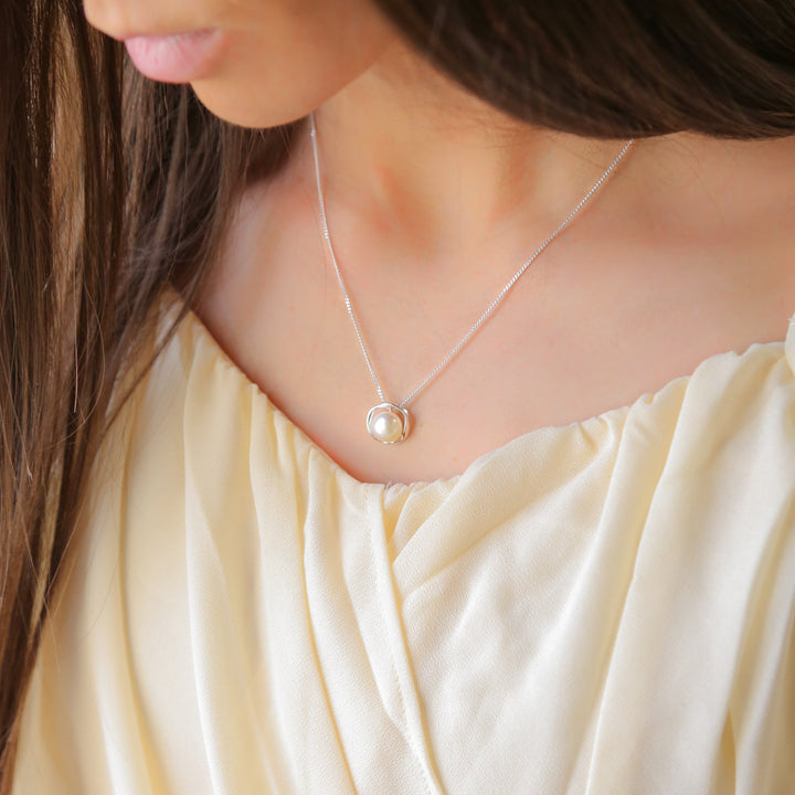 a woman wearing a necklace with a pearl on it