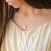 a woman wearing a necklace with a pearl on it