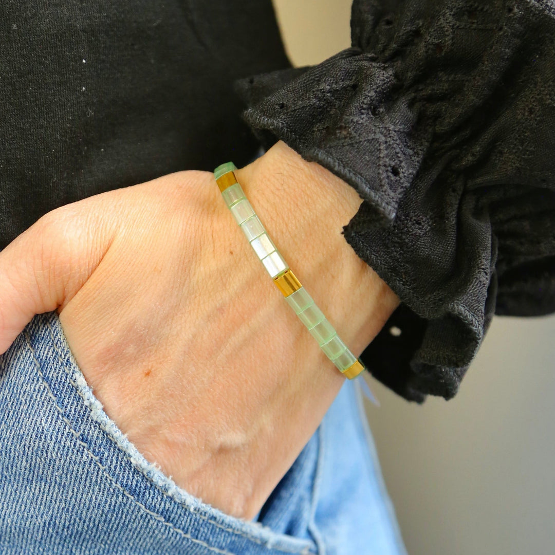 a woman wearing a green bracelet with a gold bar