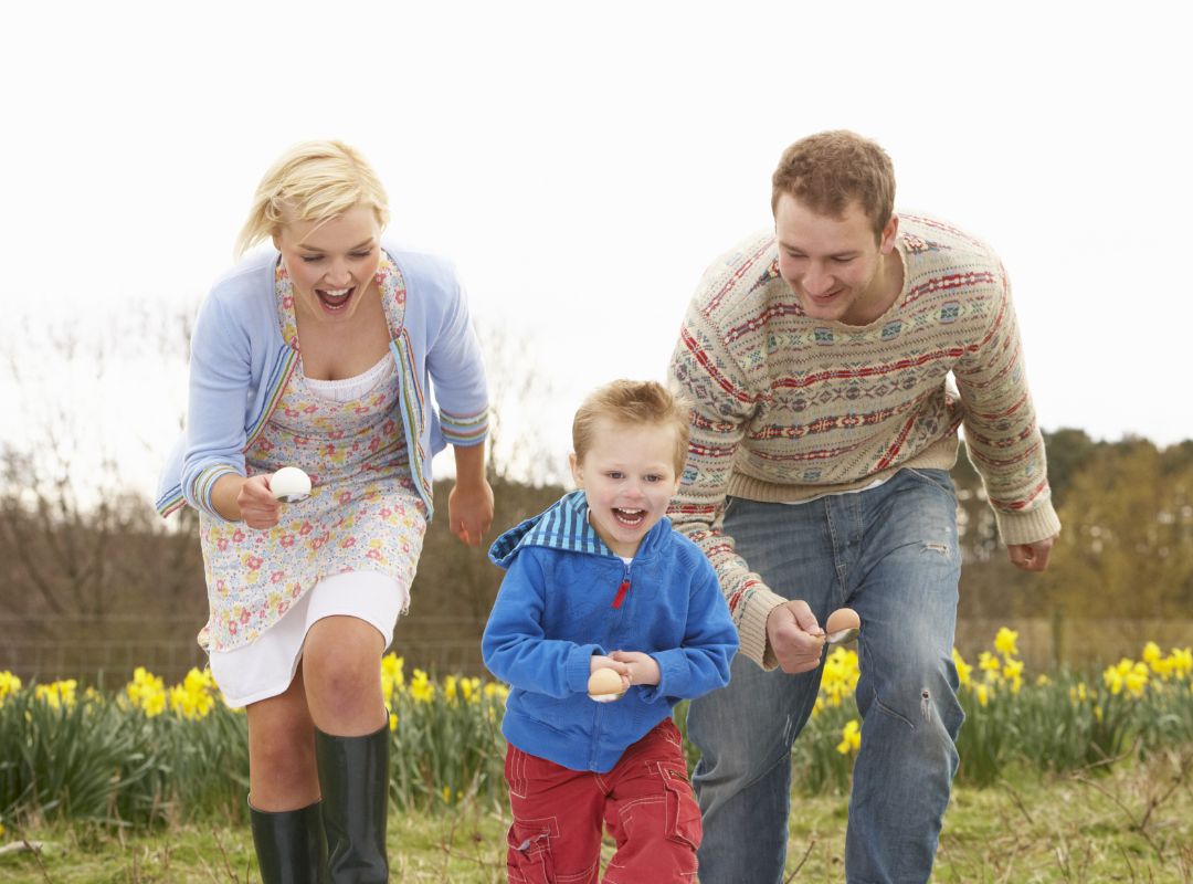 There is a family doing an egg race with flowers behind them.