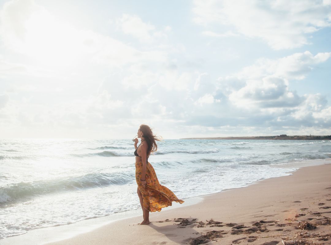 There is a woman in a yellow skirt and swim suit on a beach.