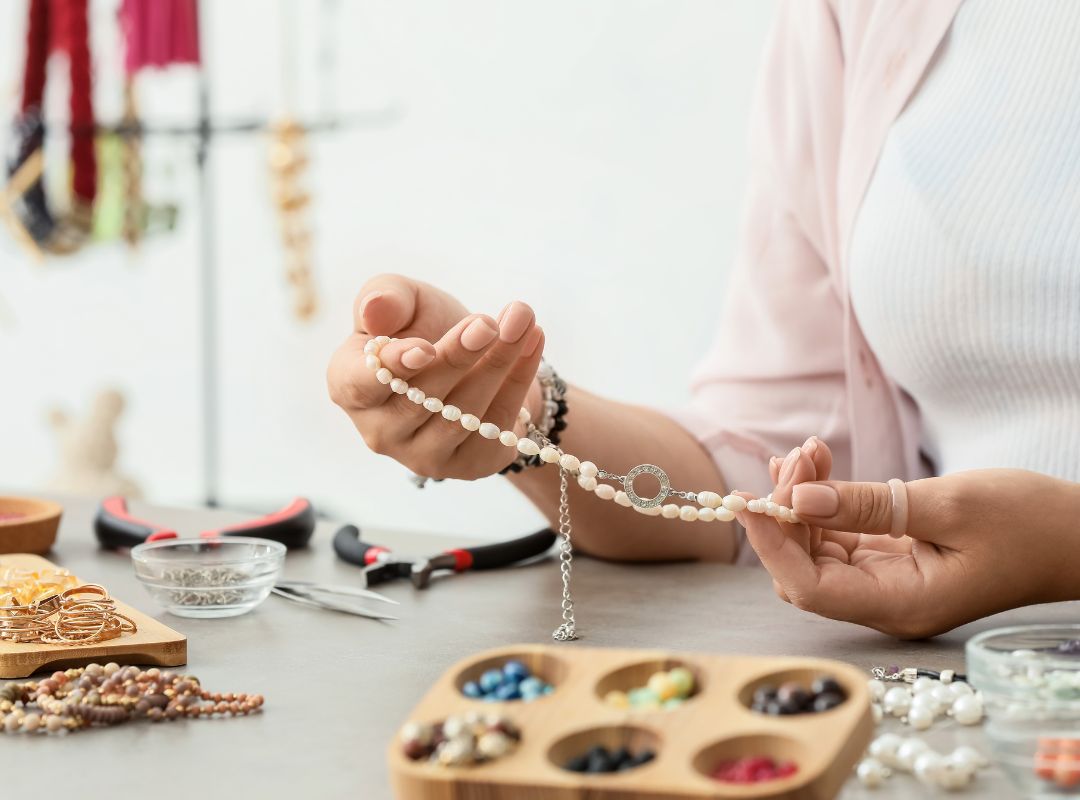 There is a woman making bracelets with a bracelet making set up around her.