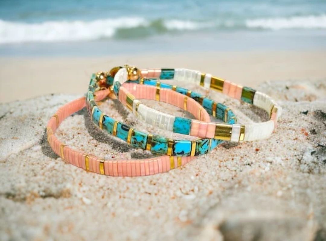 There are three bracelets of pink, blue, and white on a beach.