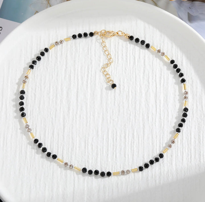 a black and gold beaded necklace on a white plate