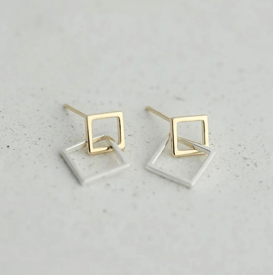 a pair of gold and silver earrings on a white surface