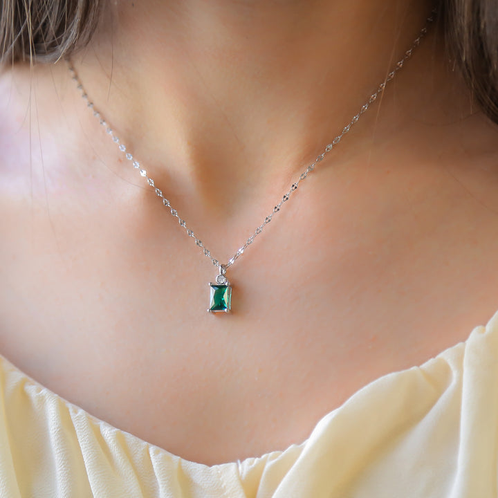 a woman wearing a necklace with a green stone