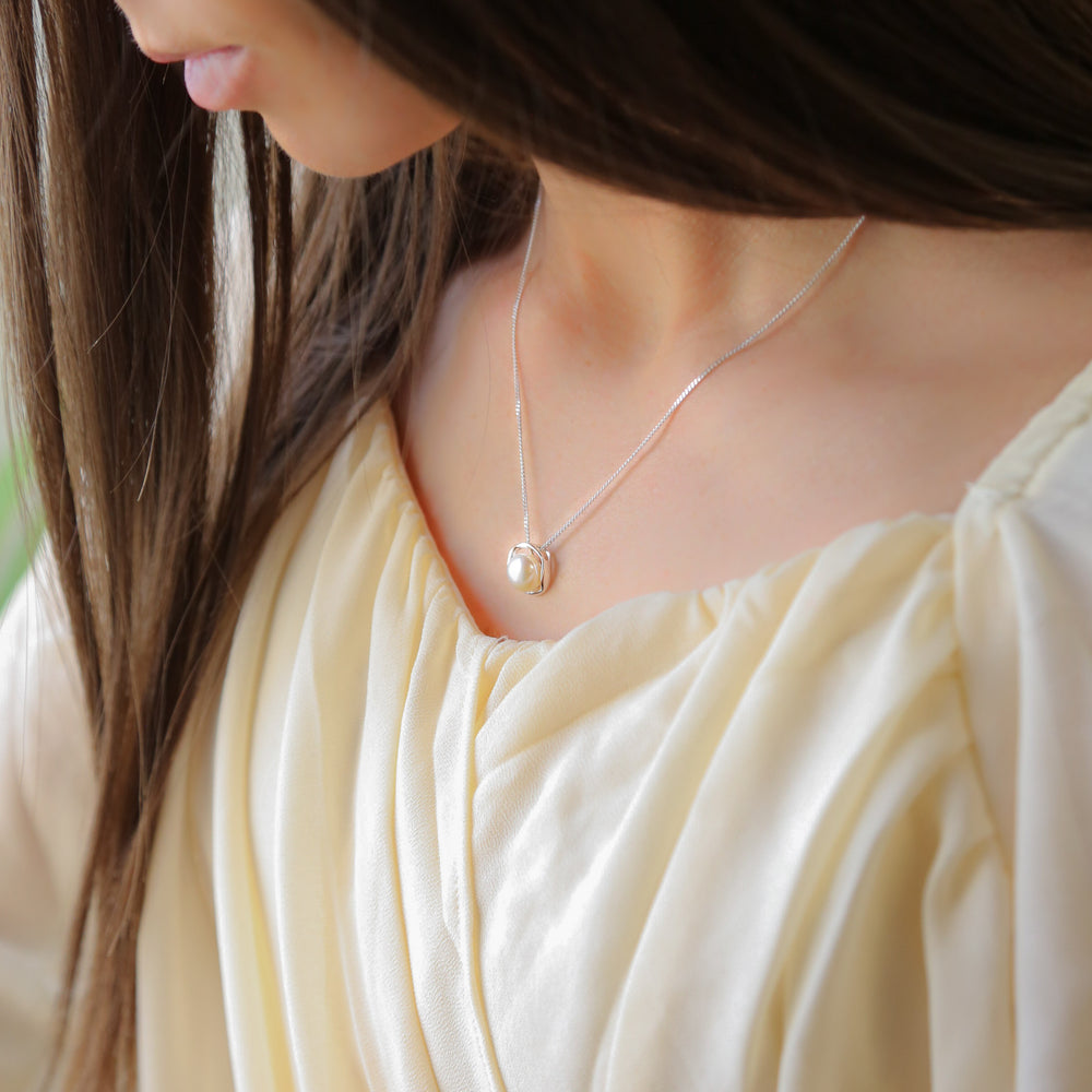 a woman wearing a necklace with a pearl on it