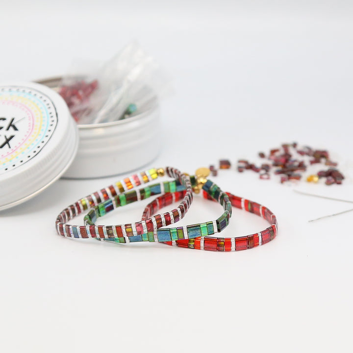 Colorful beaded bracelets on a white surface with a small container in the background.