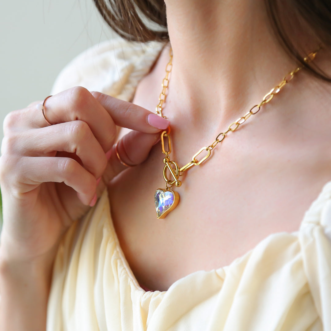 a woman wearing a gold necklace with a heart charm