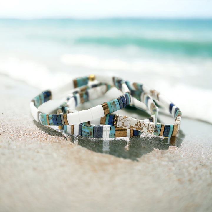 a couple of bracelets sitting on top of a sandy beach