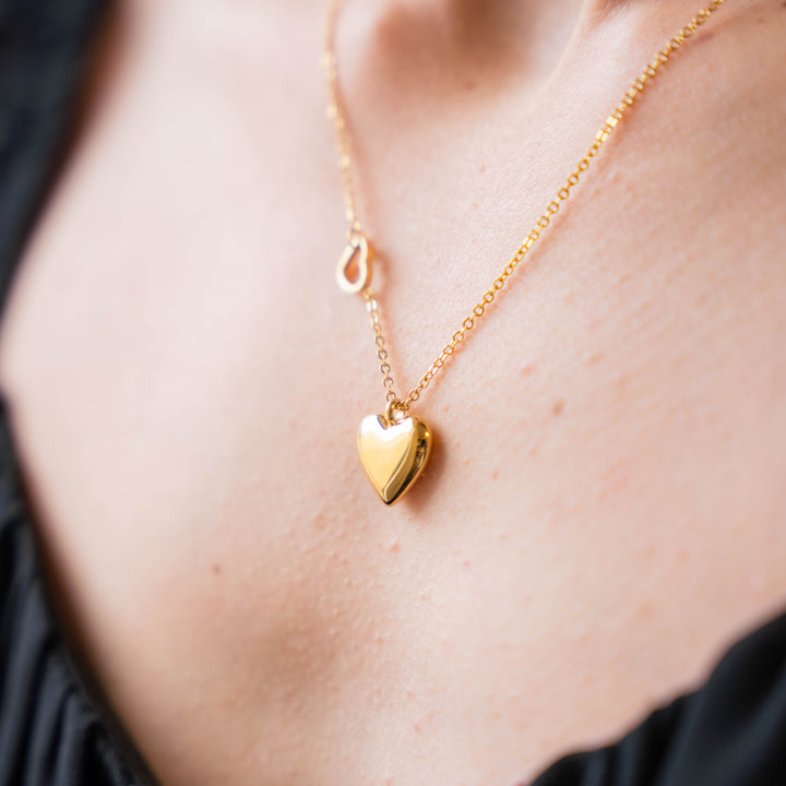 a close up of a woman wearing a gold heart necklace