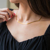 a woman in a black top is tying a gold necklace