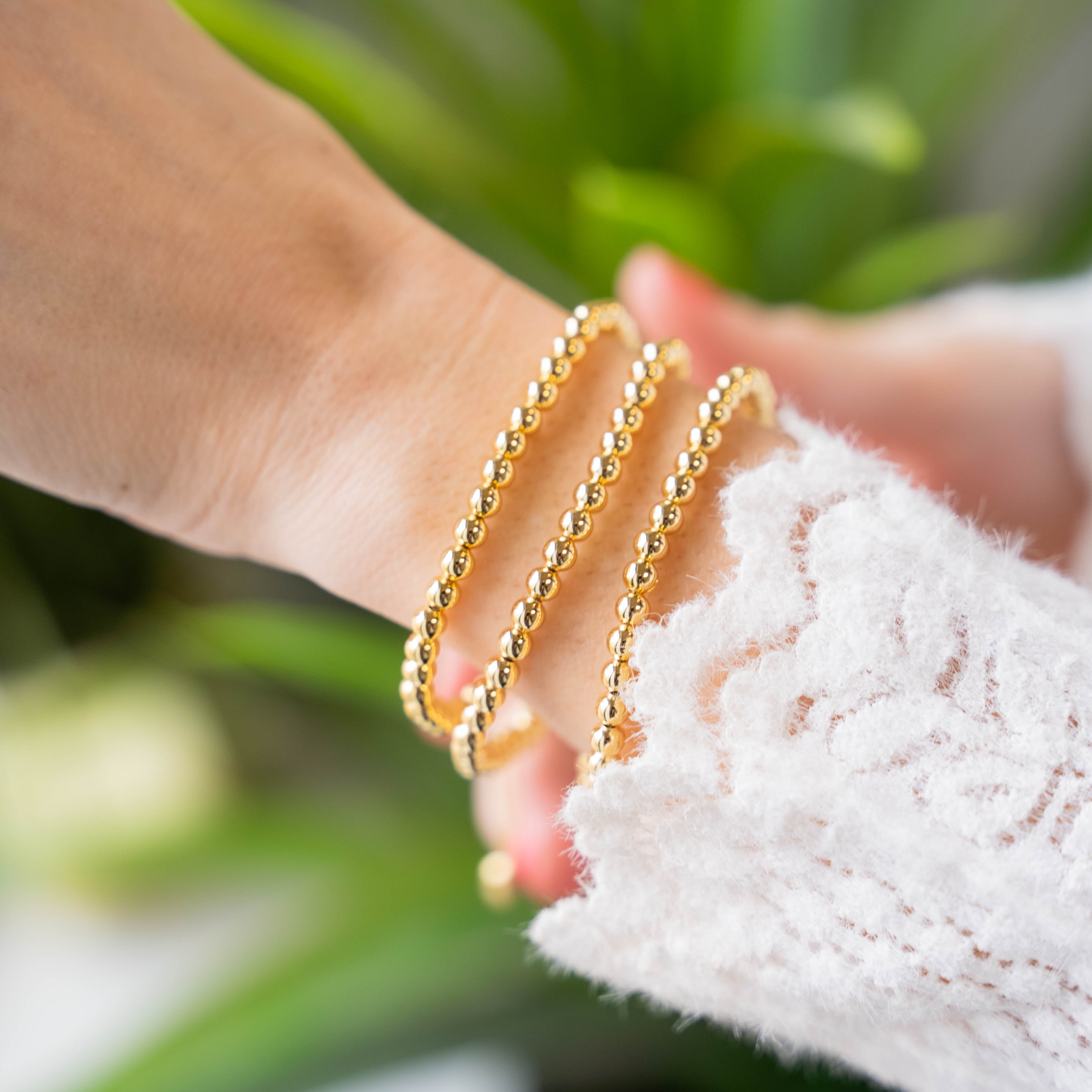 a woman's hand holding a gold beaded bracelet