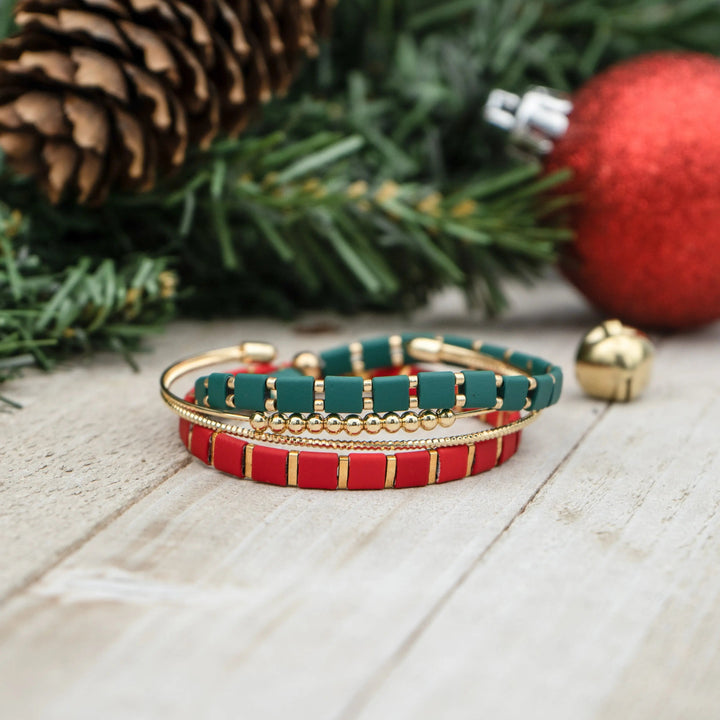 a red and green bracelet sitting next to a christmas tree